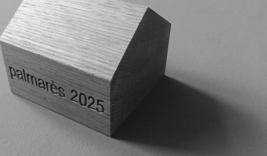 Maison en bois sur laquelle est écrit "Palmarès 2025". Photo en noir et blanc