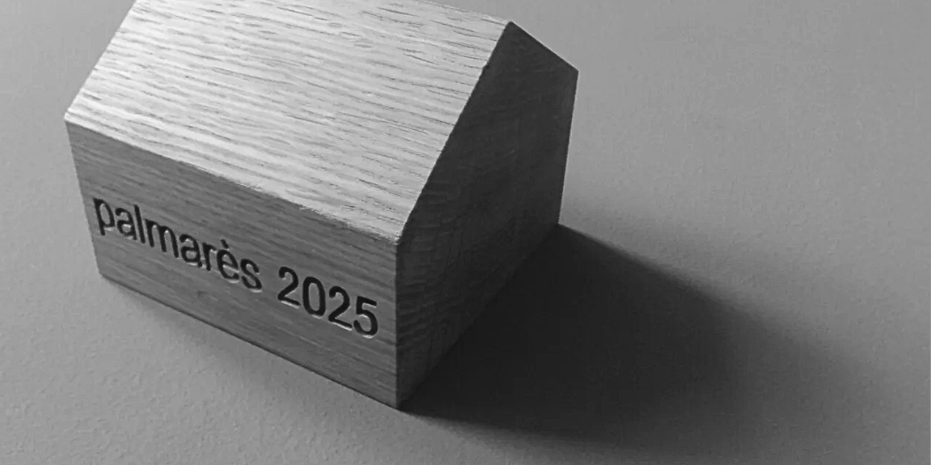Maison en bois sur laquelle est écrit "Palmarès 2025". Photo en noir et blanc